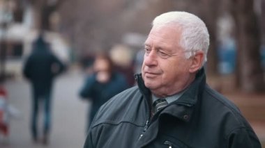 Üst düzey bir adam sobebody bir park sokaktaki insanlarla dolu gri başlı adam bir ağır zipup ceket giymiş etkileyici bir manzara sonbahar bekliyor. O passerbies tam bir park sokakta duruyor ve sonbaharda görünüyor 