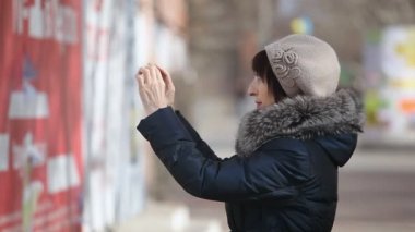 Akıllı orta yaşlı bir kadın bir şehir sokak esmer bir orta yaşlı kadın bir fotoğraf bir duvara yapışır bir heyecan verici görünümünü kağıt reklam ile kaplı bir fotoğraf bir reklam alır. O profilde sonbaharda standları.