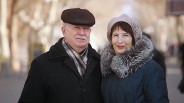 Mutlu bir aile stand ve neşeyle bir park sokakta gülümsemek güneşli bir sonbahar içinde cesur kıdemli biri ve şık bir orta yaşlı kadın ayakta ve mutlu bir pitoresk park sokakta sonbaharda gülümseyen iyimser bir bakış.