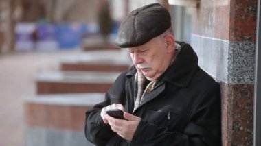 Bıyıklı bir komuta sizde duruyor ve cep telefonunu bir semt sonbaharda cadde üzerinde bir akıllı gri saçlı adam düz kapak daimi bir şehir sonbaharda sokak mermer duvara yakın bir özgün görünümüne çevirir. O cep telefonunu arar.