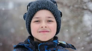 Karlı bir kış A pozitif closeup topları ve mavi bir parka ile örme şapka içinde küçük bir çocuk parkında bir sıcak örme şapka gülümsüyor neşeli bir çocuk. O durgunluk ve kışın karlı bir sokakta gülümsüyor. 