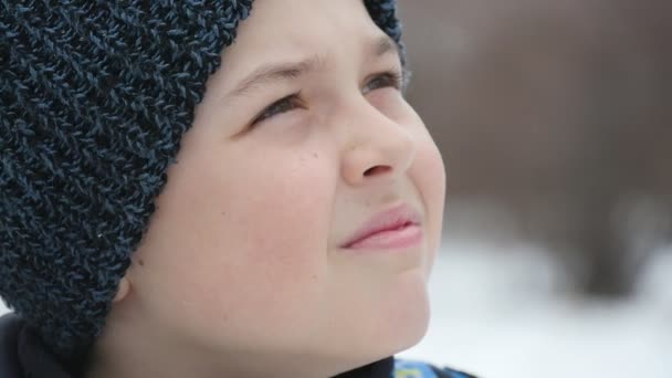 一个好奇的男孩在小巷里看着 飘落的雪花在冬天是灿烂的 一个九岁的男孩在黑色的针织帽子鼓舞人心的特写 他在冬天的雪巷里看着童话般的雪花 — 图库视频影像