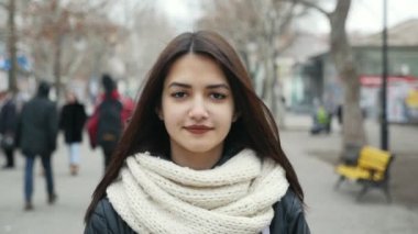 Çekici bir kız bir şehir sokak ve gülümseyerek mutlu bir şekilde kışın slo-mo derin gözlü bir güzel kız kim bir şehirde sokak parklarla çekici bir bakış ve gülümser obscurities kışın ağır çekimde yürür