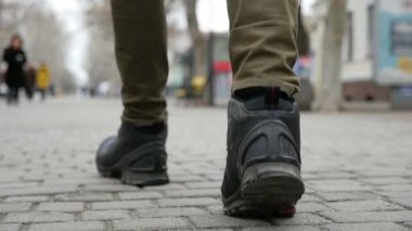 Bir closeup Çinili şehir yavaş kışın sokak üzerinde yürüyen genç bir adamın ayak özgün bir görünümü slo-mo kışın kiremitli bir cadde boyunca gidiş genç erkek hissediyorum. Trendy siyah çizmeler ayaklar.  