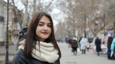 Neşeli bir kız bir park alanı ve gülümser hafif kış slo-mo şık uzun bağsız kıl gülümseyen bir kızla romantik bir bakış duruyor. O bir siyah parka ve beyaz kaşkollu giymiş. O parkta standları.    