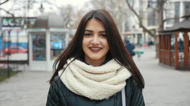 一个快乐的女孩站在城市的街道上 在冬天快乐地微笑着 在斯洛伐克 一个乐观的看法 一个华丽的女孩与深的眼睛微笑在街上 在冬季慢动作 她穿着一条白色的大围巾 — 图库视频影像