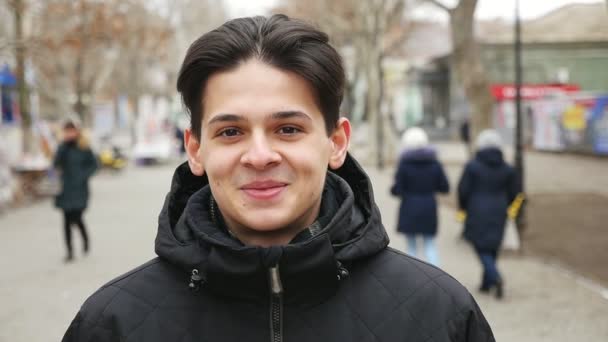 英俊的年轻人站在街上 Smails 在冬天愉快地在斯洛伐克 莫一个乐观的看法 一个时髦的年轻男子在一个黑色的大衣站在城市街道上 并微笑着开放 在冬天的斯洛伐克 — 图库视频影像