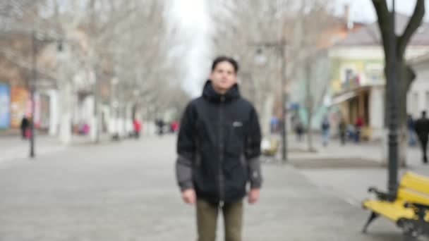 一个运动的年轻人在黑色的毛皮大衣漫步在一个小巷在冬季慢动作一个时髦的年轻人的原始看法 一个时髦的发型 在冬季沿着公园胡同慢动作 他感觉很好 — 图库视频影像