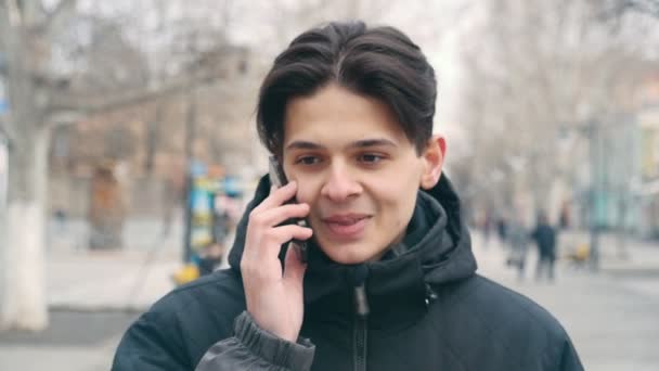 Smiling Young Man Talks Mobile While Walking Street Slo Optimistic — Stock Video