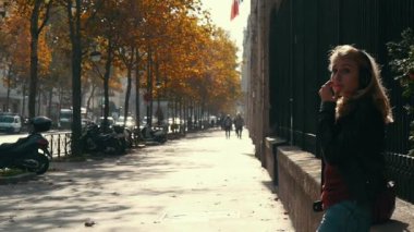 Paris, Fransa - 3 Kasım 2017: Bir rüya gibi sarışın kadın ağır çekimde Sonbaharda Paris'te pitoresk bir sokak papapet oturan uzun gevşek saç kulaklıklarla.