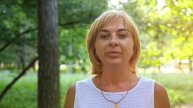 Yavaş yavaş yaz aylarında güneşli bir günde güzel bir yeşil parkta geziniyor kolsuz beyaz elbiseli güzel sarışın bir kadın portresi yeşil bir parkta bir yol boyunca bir ince sarışın kadın gider