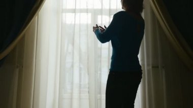 İnce bir kadın için bir pencere gelir ve ayrı yavaş çekimde bir ince kadın pantolon ve kazak için bir pencere geliyor ve beyaz perde yavaş rahat bir oda ayrı çizim sanat konusunda hava atan bir görünümünü perdeleri çizer