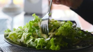 Taze yeşil salata bir plaka üzerinde olmasıdır. Bir el bir çatal ile delip geçiyor. Lezzetli görünüyor closeup düz bir tabak dolusu taze yeşil salata. Bazı el al için metalik çatal kullanır. Arka planda windows vardır.
