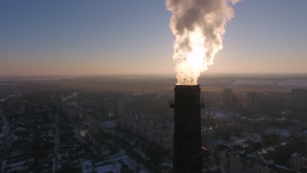 冬の夕暮れ時のウクライナの Multistoried 建物で濃厚な輝く煙の巨大な冷却煙突の日没の概観図ビューで雪に覆われた街で煙を探している白炎と高管の空中ショット — ストック動画