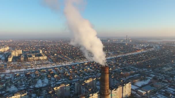 Aerial shot of high heating tube with dense smoke in city in snowy winter A bird`s eye view of a high cooling chimney with dense white smoke between multistoried buildings in Ukraine. The drone flies away — Stock Footage Aerial Shot High Heating Tube Dense Smoke City Snowy Winter Royalty Free Stock Footage