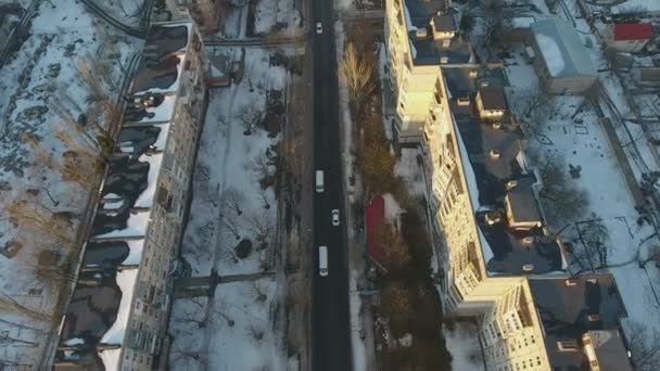 空中拍摄的雪街与汽车在 Multistireyed 大厦之间的一条惊人的鸟瞰城市道路上覆盖着雪在冬季 在冬天的两行建筑中 小汽车沿着它行驶 — 图库视频影像