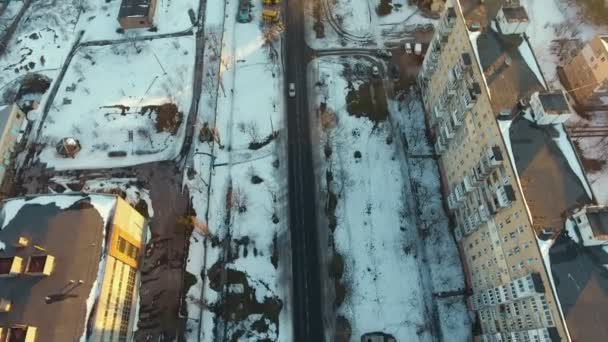 空中ショット Multistireyed の建物の中に車を移動すると雪に覆われた通り市道の元の鳥の目のビューは 冬に雪で覆われて 小型車にコンクリートの Multistroreyed の建物の中に沿って行く — ストック動画