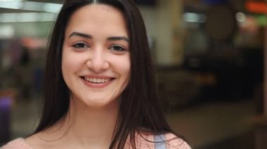 Modern bir alışveriş ayakta ve mutlu bir şekilde cam gibi bir alışveriş merkezinde sonbaharda gülümseyen uzun bağsız kıl ile iyimser ve güzel bir genç kadın portresi sonbaharda içinde mutlu neşeli genç kadın gülümsüyor. 