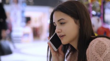 Bir süpermarkette profil bir akıllı telefon tutmak ve onun tatlı çocuk bir süpermarkette konuşmaya uzun bağsız kıl ile güzel bir genç kadının erkek arkadaşı ile onun smartphone üzerinde şık genç kadın görüşmeler. İyimser bakıyor