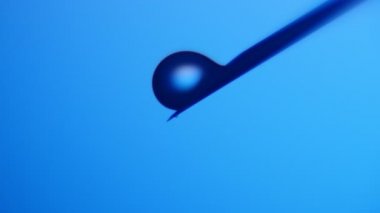 Küçük su blobs metalik bir iğne üzerinde büyük al ve kimyasal bir laboratuarda heyecan verici bir makro atış metalik bir iğne üzerinde şişlik ve bir kimyasal laboratuvar mavi arka planda gelen küçük damla düşmek