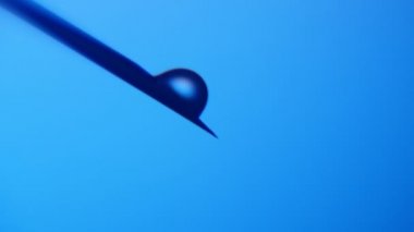 Küçük su damlaları metalik bir iğne üzerinde büyük al ve kimyasal bir laboratuarda metalik bir iğne üzerinde şişlik ve bir kimyasal laboratuvar mavi arka planda düşen küçük küçük bir etkileyici makro çekim düşmek