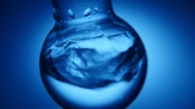 Crystaline su kimyasal laboratuvar yuvarlak bir şişesi içinde azgın bir kimya laboratuarında zor sarsılmış bir yuvarlak şişesi suda bir arty makro çekim zor sarsıldı. Köpüklü su karanlıkta atış mavi arka plan olduğunu