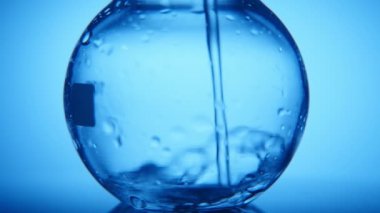 Büyük yuvarlak şişesi crystaline su mavi arka planda dar bir akışı bir etkileyici makro çekim bir büyük yuvarlak cam şişesi dolu bir kimyasal laboratuvar distile su ile doldurulur 