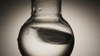 Temiz su kimyasal laboratuvar bir yuvarlak alt şişesi içinde bir yuvarlak alt şişe temiz suda bir retro makro çekim ıslak noktalı gri arka planda bir kimyasal laboratuvar sarsıldı bükülmüş.