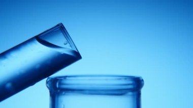 Temiz su dar bir tüp geniş bir iki test tüpleri birbirine dokunmadan bir kimyasal laboratuvar A şık makro çekim içine dökülür. Kristal berraklığında su akar geniş bir mavi arka planda dar bir tüp