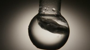 Crystaline su kabarcıkları ile tıbbi laboratuara bir yuvarlak alt şişesi içinde tıbbi laboratuarda sarsılmış bir yuvarlak alt şişe temiz suda bir vintage makro çekim sarsıldı. Su beyaz ve gri gölgeler ile oynar.