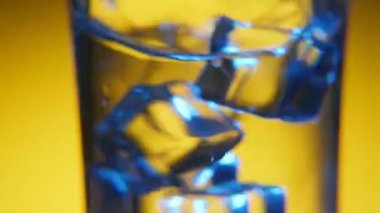 Beş buz küpleri beş buz küpleri ile sıvı serinletici bir şeffaf cam sarsılmış bir harika makro çekim kabarcıkları ile kaplı sarı arka planda kristal-açık bir cam ve su sıçramalarına Studio sarsıldı