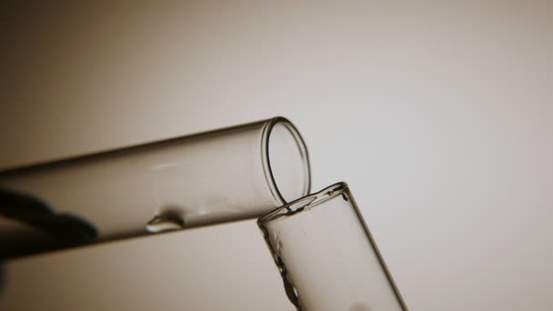 清洁水从一个样品管倒入另一个在化学实验室一个复古的宏观拍摄两个试管互相接触 在灰色背景下 清澈的水从一根管子流向另一管 — 图库视频影像