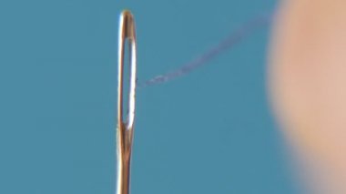 Terzinin parmak mor bir iş parçacığı bir menekşe pamuk dize bir delik gri ve mavi bir stüdyoda dikey bir iğne içine koyarak terzi'nın parmakları bir gri-mavi stüdyo A vintage makro çekim bir iğne deliğe itmek