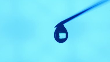 Bir damlacık su bir iğne ucu üzerinde büyür ve düşüyor. Bu su içinde yanan bir delik olan şeffaf bir blob sanatsal bir makro içinde ışık var. Turkuaz aboratory içinde aşağı su kitapçık küçük.
