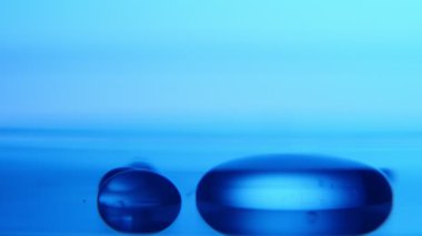 Su küçük cam gibi bir alan üzerine düşmek ve düşen su bir etkileyici makro çekim bir tıbbi laboratuvar mavi arka planda küçük bir şeffaf havuz yapım damla bir laboratuvarda bir küçük dairesel pubble formu. 
