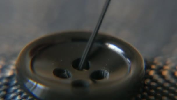ダーク素材ボタンを縫い付けます 黒糸と針は黒糸で大きな針を使用して厚物素材を見ていくつかのレトロ縫い つの穴で黒ボタンの印象的なマクロを撮影しました — ストック動画