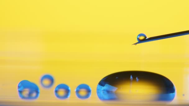 水の小さなちびりちびり注射器から落ちるし 金属針から液体 Dribling のおしっこの滴の小さなプール の陽気なマクロを作るとラボの黄色の背景に大きな丸いプールに滑りをロール — ストック動画