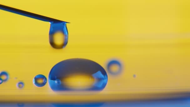透明な水滴がガラス表面に金属針から落ちて 黄色ラボで小さな水たまりを作って華麗な水滴の印象的なマクロ小さなプールを形成 注射器から滴します — ストック動画