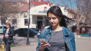 Güzel kız bir smartphone ile güneşli bir günde bahar slo-mo yürüyen bir şık genç kadın etkileyici bir manzara gider ve net tutma sörf bir smartphone ona el ağır çekimde rüzgarlı havalarda