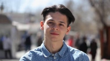 Hoş genç adam standları ve gülümsüyor neşeyle bir şehirde sokak bahar bir pamuklu gömlek ayakta ve romantik bir şehirde güneşli bir günde sokak gülümseyen crewt saç kesimi ile mutlu bir genç adam portresi
