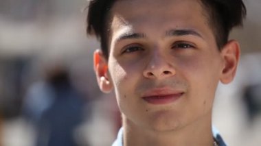 Genç adam standları ve iyimser bir şehirde güneşli bir günde sokak bahar Bokeh portre mutlulukla gülümseyerek kısa saç kesimi ile şık genç bir adam gülümsüyor ve bahar güneşli bir günde sokak şehirde ayakta