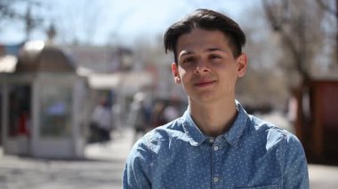 Genç adam standları ve neşeyle bir şehirde güneşli bir günde sokak bahar Bokeh portre iyimser bir gencin mutlu bir şekilde gülümseyerek mürettebat saç kesimi ile gülümsüyor ve bahar güneşli bir günde sokak şehirde ayakta