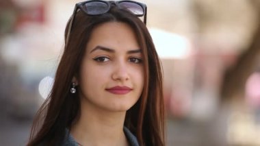 Güzel kız hafifçe gülümsüyor ve içtenlikle gülümsedi ve onun uzun bağsız kıl bir arka sokakta sırayla güneşli bir günde baharda koyar bir romantik kadın güneş gözlüğü ile portresi güneşli bir şehir sokakta smartens