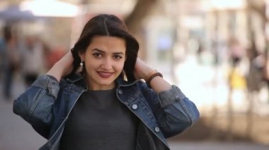 Gülümseyen genç kadın esmer saçlarını bir şehir salonu sırada bahar smartens ve onun uzun bağsız kıl inan sokak güneşli bir günde baharda önemser neşeli ve güzel genç bir kadın portresi koyar