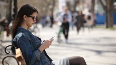 Başarılı kadın onun smartphone cep telefonu ile bir sokak profili çekici bir genç kadın, onun cep net tarama ve bahar güneşli bir günde güzel bir arka sokakta bir bankta oturan gözlüklü banktaoturuyor net sörf