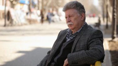 Bilge bir adam beyaz bıyıklı bir bankta oturur ve beyaz bıyıklı bir bankta oturan ve bir arka sokakta onun cep güneş gözlüğü dışında baharda alarak kendine güvenen bir komuta sizde profili güneş gözlüğü çeker
