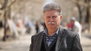 Bıyıklı güvenen bir yaşlı adam düşünüyor ve bahar bahar ciddi bir üst düzey adam gri ceketli beyaz bıyıklı Bokeh portre görkemli sokak güneşli bir günde bir ara sokakta duruyor