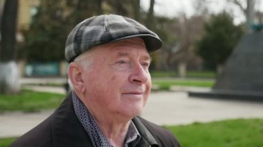 Bilge adam oturma ve yeşil bir arka sokakta zor hayatı bahar A 180 derece yeşil çim bir arka sokakta bir bankta bahar güneşli bir günde oturmuş bir chechered kap içinde üst düzey bir adam çekim düşünüyorum