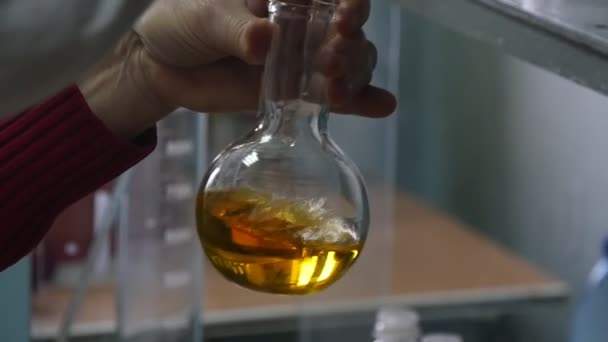 科学家用 Goldenl 液体在生物技术实验室中旋转一个玻璃烧瓶 一个引人注目的观点是一个在现代生物技术实验室中由男性手扭曲的圆形玻璃瓶瓶 污染水平测量 — 图库视频影像