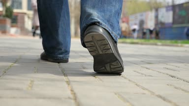 Erkek siyah ayakkabı ayaklarda şehir kaldırım boyunca adamın hissediyorum mavi kot pantolon ve siyah ayakkabılar bahar slo-mo güneşli bir günde bir şehir kaldırım boyunca gidiş bir etkileyici bokeh çekim bahar yavaş yürümek
